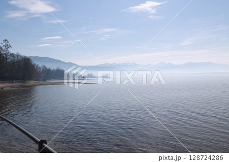 A calm lake with a few trees in the background 128724286