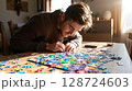 A person focuses intently while assembling a colorful jigsaw puzzle indoors 128724603