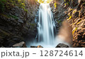 Majestic waterfall cascading down rocky cliffs in a sunlit forest at dawn 128724614