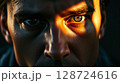 A close-up portrait of a man with intense eyes illuminated by dramatic lighting 128724616