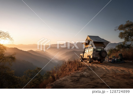 Off-road camper with rooftop tent parked on a cliff edge at golden sunrise, overlooking misty mountains and embracing remote travel freedom 128724899