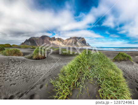 Astonishing sunny day and gorgeous rippled black sand beach with dunes and green grass on Stokksnes cape in Iceland. Astonishing sunny day and gorgeous rippled black sand beach with dunes and green grass on Stokksnes cape in Iceland. 128724961