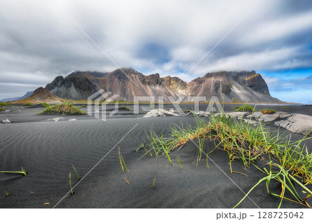 Amazing sunny day and gorgeous rippled black sand beach with dunes and green grass on Stokksnes cape in Iceland. 128725042