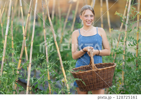 Young woman with basket in cottage garden 128725161