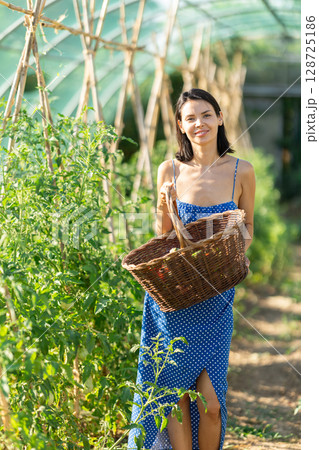 Young girl with basket is working in greenhouse between beds 128725186
