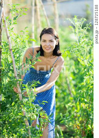 Girl farmer staff takes care of plants, ties up climbing garden fruit crops Girl farmer staff takes care of plants, ties up climbing garden fruit crops 128725188