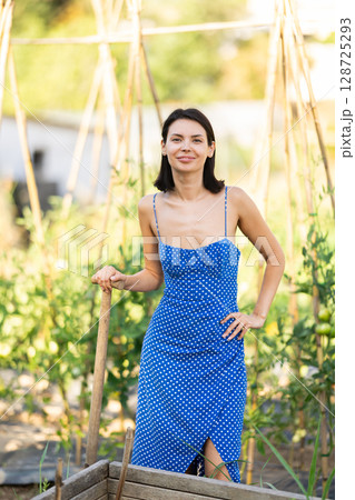 Rural dweller girl in straw hat with watering can against background of vegetable beds 128725293