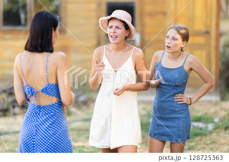 Three young women neighbors quarrel and swear in rural yard 128725363