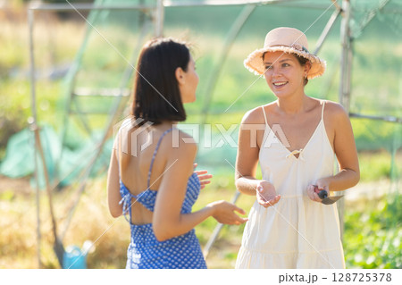Two women talking in garden greenhouse 128725378