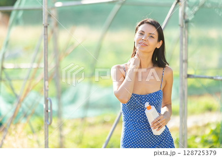 Adult woman applying sunscreen in garden greenhouse 128725379