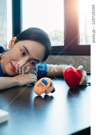 A woman gazes at brain and heart models on a table, symbolizing the balance between emotion and intellect. A woman gazes at brain and heart models on a table, symbolizing the balance between emotion and intellect. 128726384