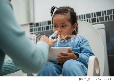 mother making nasal wash for toddler girl with syringe and saline. cleaning nose 128727954