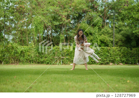 mother and toddler girl playing circling around on grass field at park 128727969
