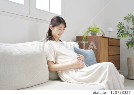 ソファーに座ってお腹を触る妊婦 128728327