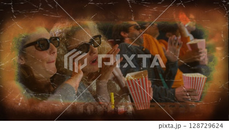 Leaning forward moviegoer friends waving hands in dark theater, with 3D glasses and popcorn buckets 128729624