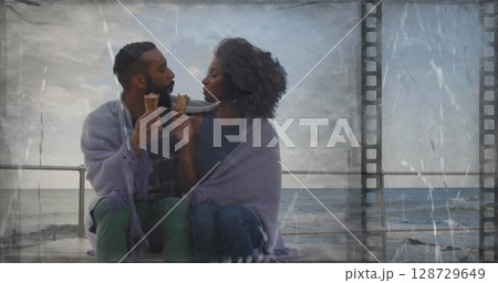 Romantic couple exchanging ice cream cones on seaside promenade, with purple blanket 128729649
