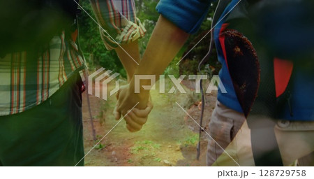 Walking couple holding hands along forest trail, with backpacks sticks and gear straps 128729758
