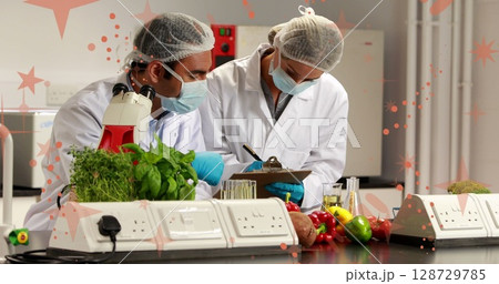 Reviewing scientists recording vegetable samples at food testing lab, with clipboard and microscope 128729785
