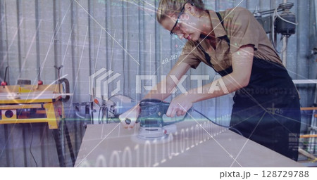 Sanding woman craftsperson using orbital sander on board in workshop, with binary graphics overlay 128729788