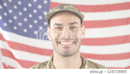 Smiling soldier in camouflage uniform and cap standing before American flag, with patriotic theme Smiling soldier in camouflage uniform and cap standing before American flag, with patriotic theme 128729805