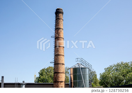Old Industrial Chimney and Metal Silo Under Clear Blue Sky in Summer Old Industrial Chimney and Metal Silo Under Clear Blue Sky in Summer 128730256