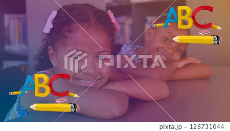 Image of letters and pencil over happy diverse girls sitting in school desks 128731044