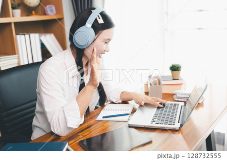 Asian girl student wear headphones learning online watching webinar class looking at laptop computer eLearning remote lesson making notes or video calling virtual conference meeting teacher at home. 128732555