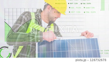 Man wearing yellow hard hat, safety vest adjusting solar panel in studio, with financial charts 128732678