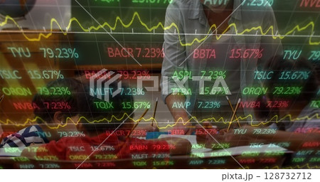 Leaning executive in gray shirt analyzing charts at office desk, with ticker overlay, copy space 128732712