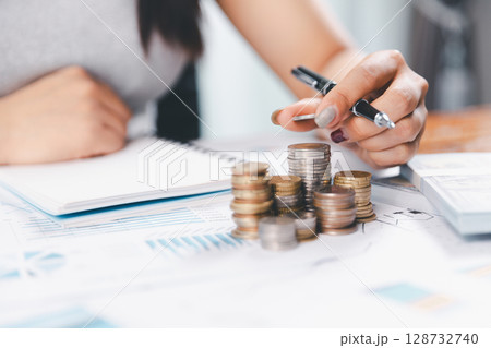 Young Asian woman making stack of coin. invest save finance concept, saving money, investment. dollar bills on table with pile of coins and banks calculator, money to save and invest to make income. 128732740