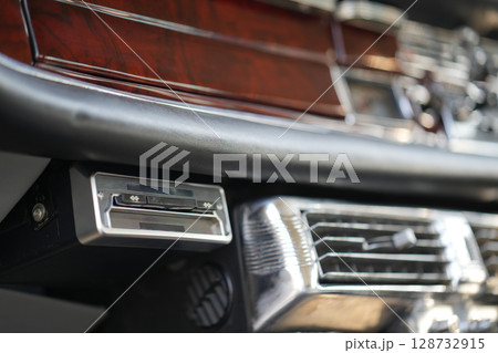 The dashboard of a vintage classic car features detailed analog gauges, a radio, and air vents in polished wood and chrome, offering a fresh yet luxurious look. 128732915