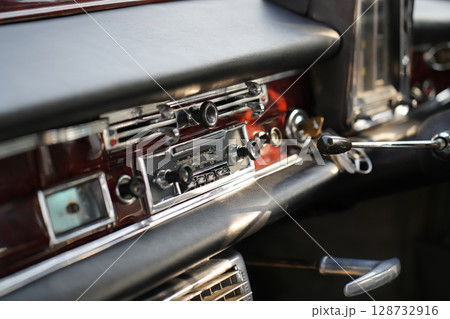 The dashboard of a vintage classic car features detailed analog gauges, a radio, and air vents in polished wood and chrome, offering a fresh yet luxurious look. The dashboard of a vintage classic car features detailed analog gauges, a radio, and air vents in polished wood and chrome, offering a fresh yet luxurious look. 128732916