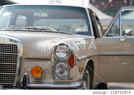 The round headlights and side turn signals on classic cars, framed in polished chrome, highlight the vintage style with old-fashioned lighting and curved fender details. 128732974