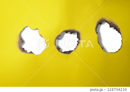 Burnt hole on a sheet of yellow paper on a white background. Copy space Burnt hole on a sheet of yellow paper on a white background. Copy space 128734210