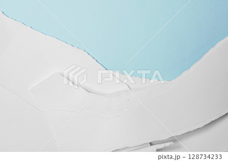 Stack of pieces of ripped and torn white paper on a blue background. Copy space 128734233