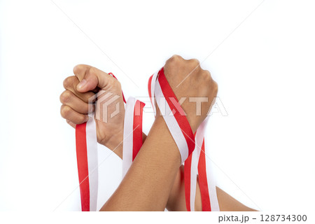 Human hand holding the Indonesian ribbon flag to celebrate Indonesia Independence Day isolated over a white background. Concept of Kemerdekaan 128734300