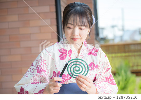 蚊取り線香に火をつける浴衣女性 128735210