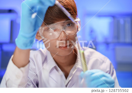 Scientists working in Laboratory using pipette dropping liquid sample into test tube. 128735502