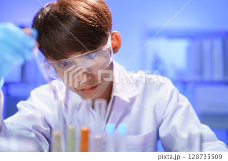 Scientists working in Laboratory using pipette dropping liquid sample into test tube. 128735509