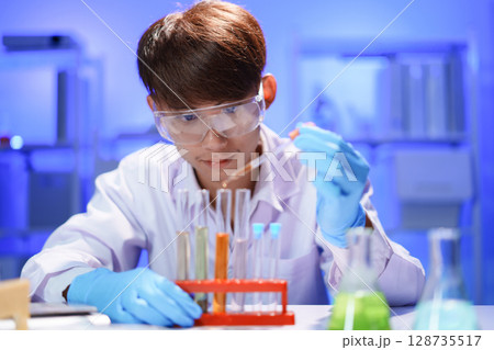 Scientists working in Laboratory using pipette dropping liquid sample into test tube. 128735517