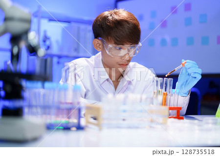 Scientists working in Laboratory using pipette dropping liquid sample into test tube. 128735518
