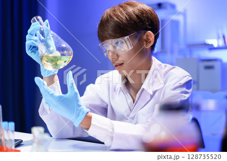 A young male scientist examining a in beaker a lab. 128735520