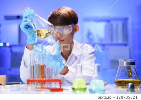 A young male scientist examining a in beaker a lab. 128735521