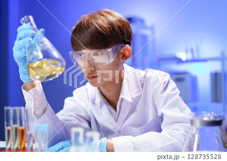 A young male scientist examining a in beaker a lab. 128735528