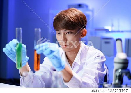 A young male scientist examining a test tube in a lab. A young male scientist examining a test tube in a lab. 128735567