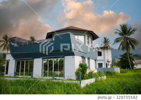 A beautifully designed contemporary home is set in nature, surrounded by palm trees and dramatic clouds above 128735582