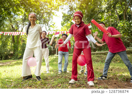 Portrait of an Indonesian southeast asian people celebrate Indonesia Independence Day on the 17th of August with a game of keep the balloon from blowing out outdoors. Concept of Kemerdekaan Indonesia 128736874
