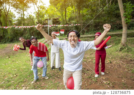 Portrait of an Indonesian southeast asian people celebrate Indonesia Independence Day on the 17th of August with a game of keep the balloon from blowing out outdoors. Concept of Kemerdekaan Indonesia 128736875