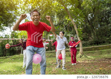 Portrait of an Indonesian southeast asian people celebrate Indonesia Independence Day on the 17th of August with a game of keep the balloon from blowing out outdoors. Concept of Kemerdekaan Indonesia 128736876