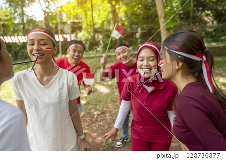 Portrait of an Indonesian southeast asian people celebrate Indonesia Independence Day on the 17th of August with a game of moving the rubber band with a straw outdoors. Concept of Kemerdekaan 128736877
